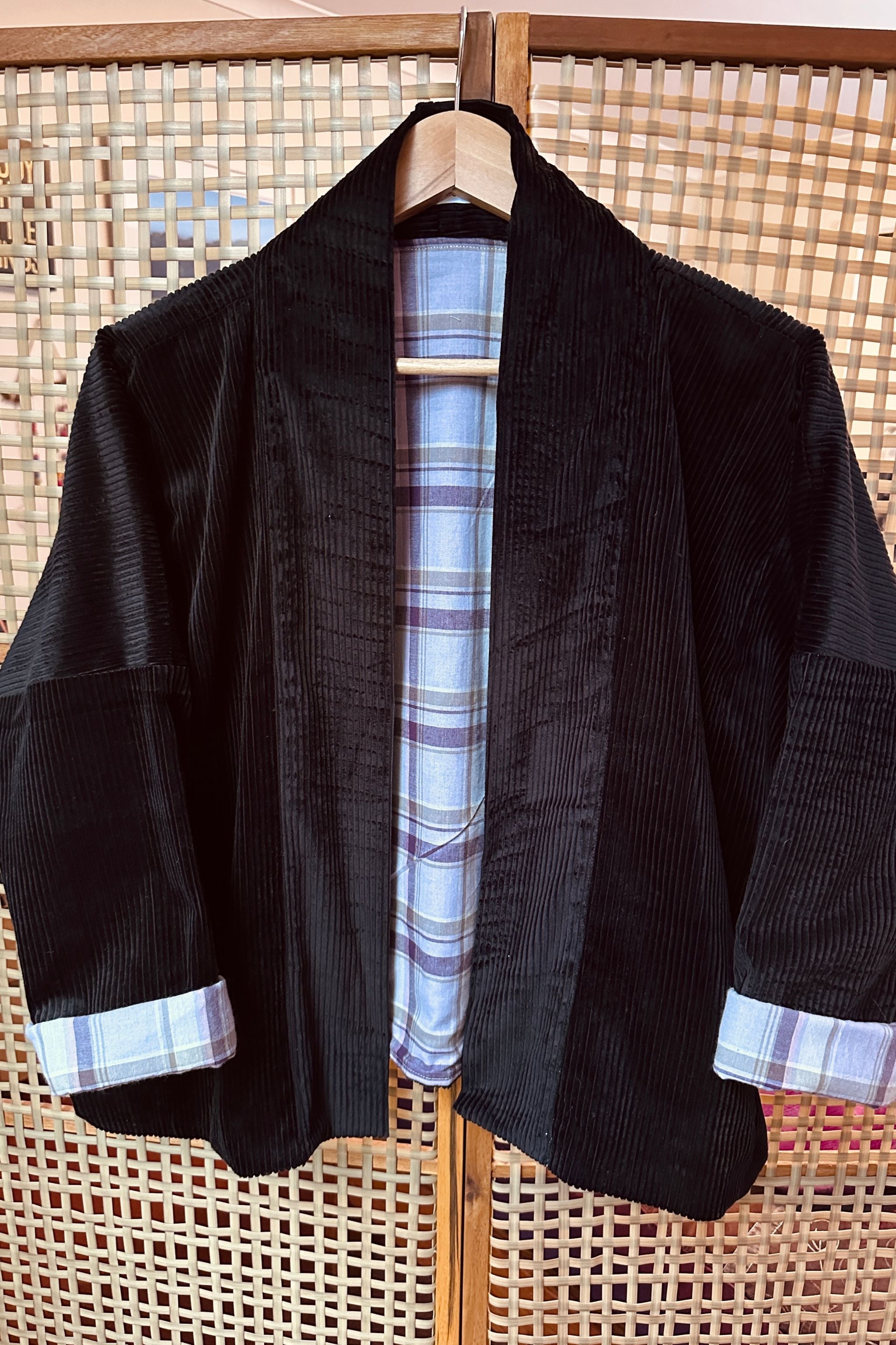 Black jacket with plaid lining and cuffs on a wooden hanger against a woven background